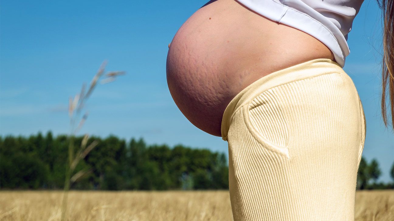 Pregnant person exposes belly in a field outdoors