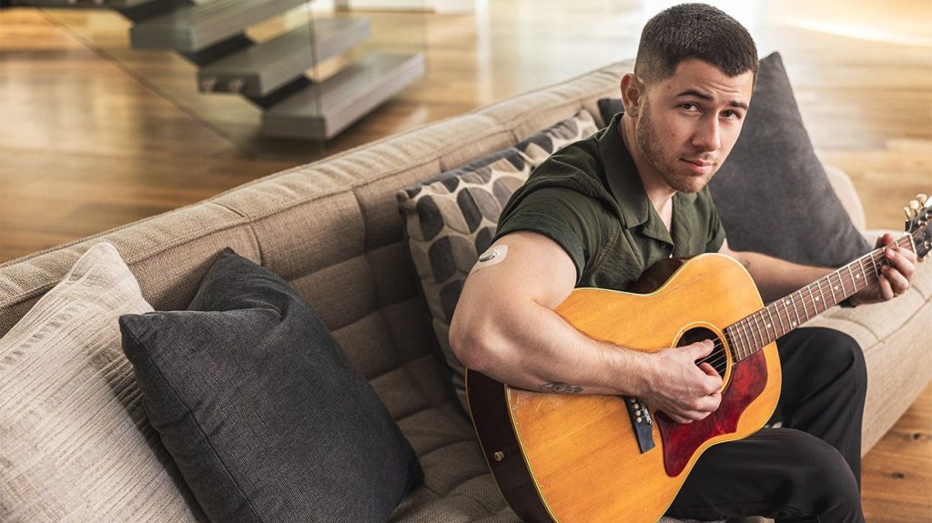 Nick Jonas sits on couch with guitar