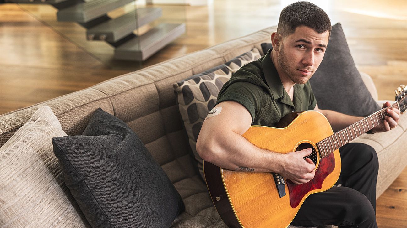 Nick Jonas sits on couch with guitar