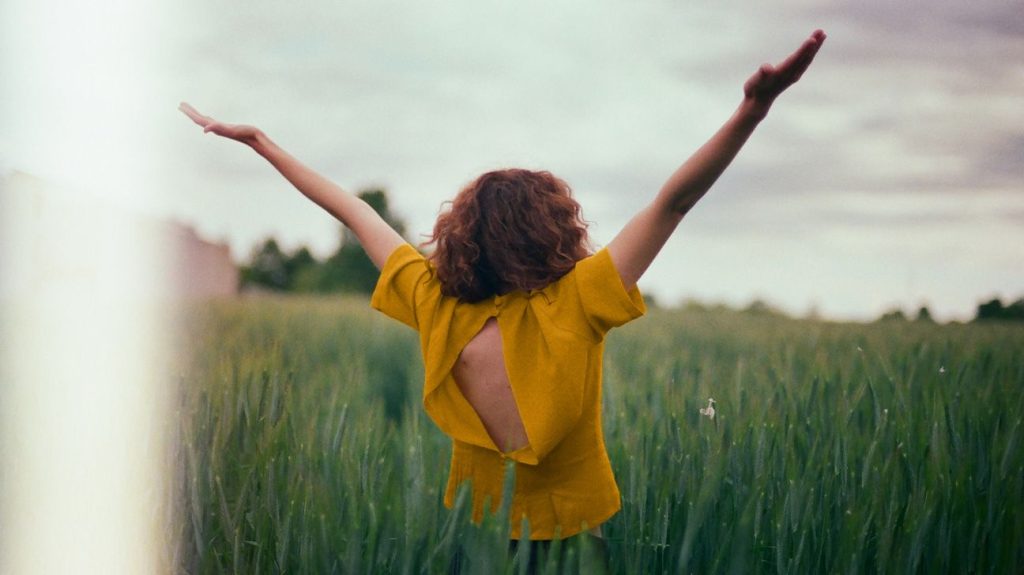 Female in a field with her arms in the air as though she is happy
