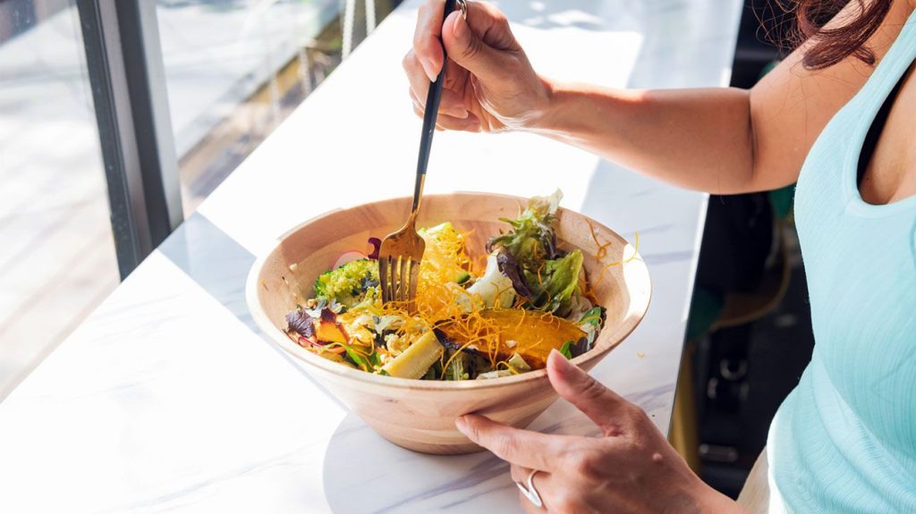 Female eating a bowl of salad by a window